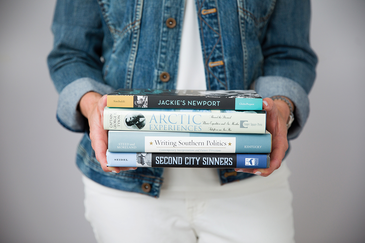 Jen Huppert holding a stack of her book cover designs in her hands with the spines facing out.